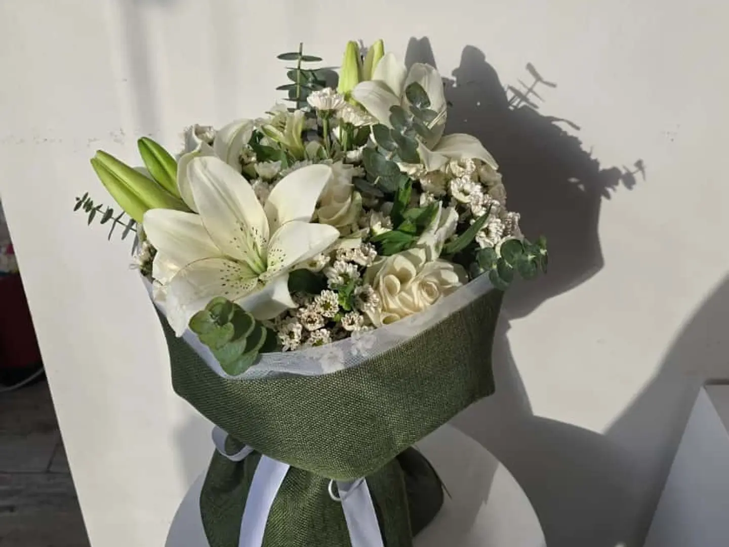 A Bouquet Of Daisies And Lilies With Olive Colored Wrapping.
