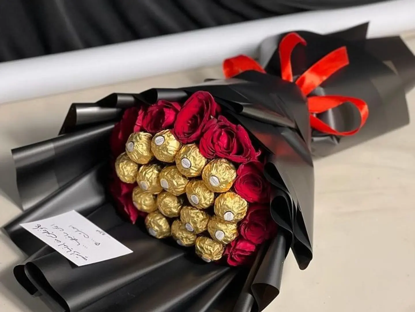 A Bouquet Of Red Roses With Gold Chocolate Balls And Black Packaging