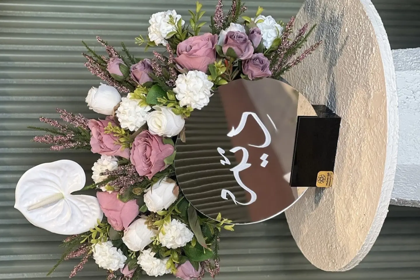 A Mirror Vase With Artificial Flowers And A Name Written On It